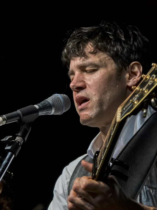 Wolf Edwards singing into a microphone while playing guitar